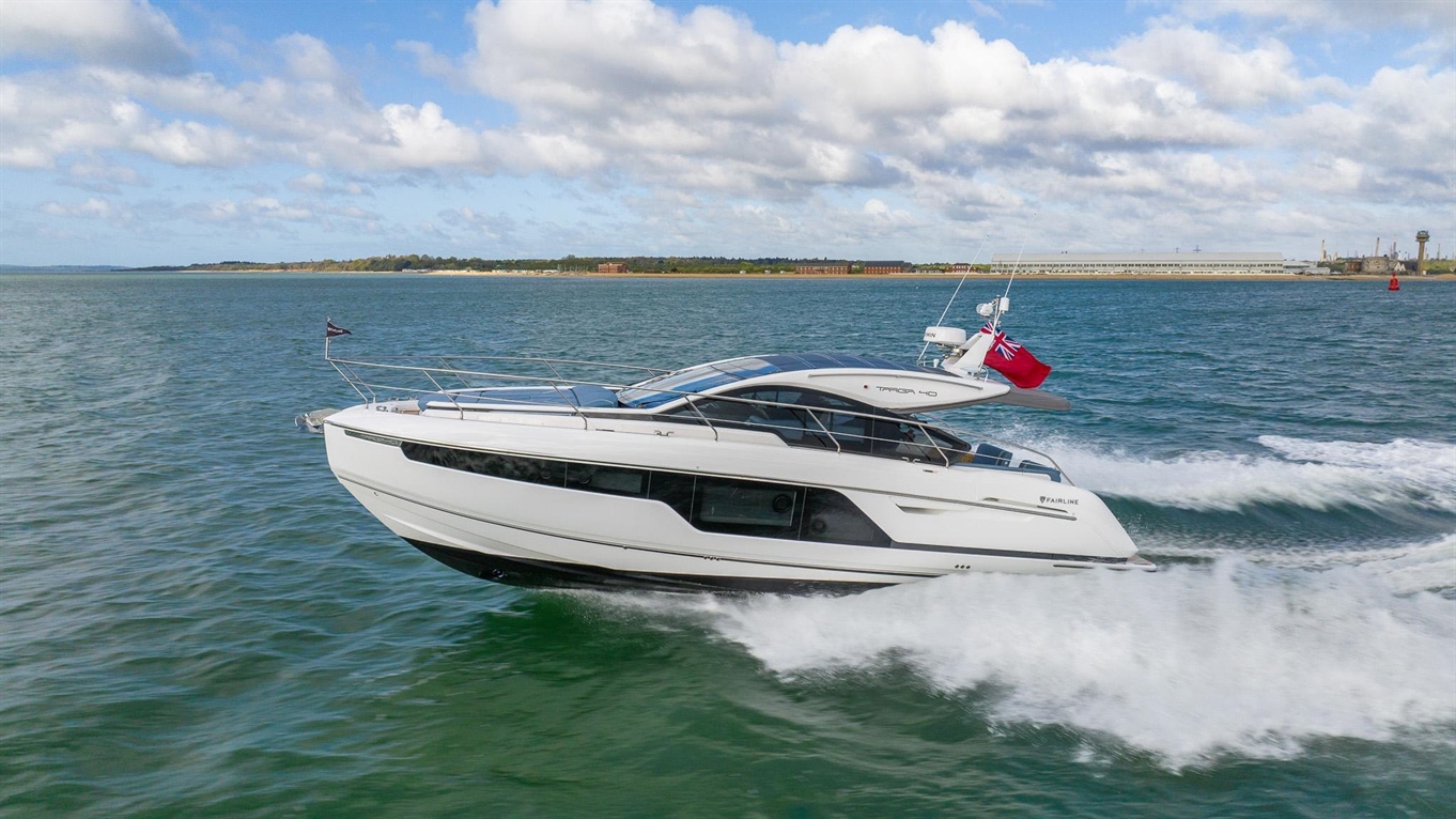 Luxury motor yacht cruising through blue waters, with a British flag visible and white cloud-filled skies in the background.